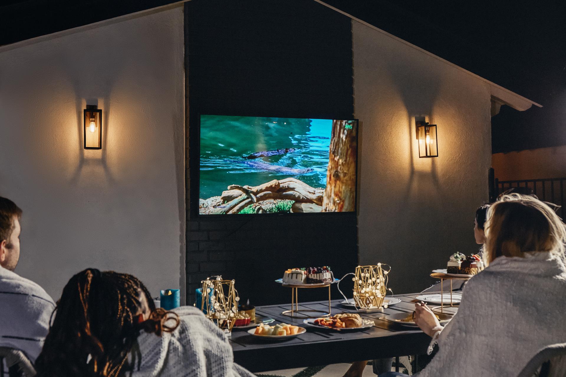 Family watching NFL game on Sylvox outdoor TV on balcony during cold weather